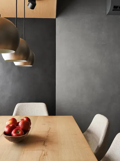 A detail from the AD House dining area, where a white ash wood table is set against black concrete walls. The contrast in materials and the warm glow of the pendant lights create an intimate and modern dining nook.