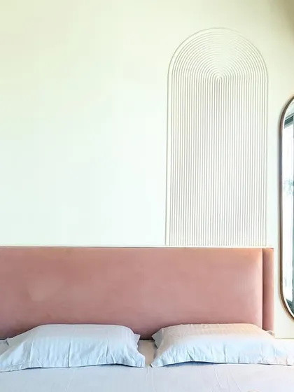 A close-up of the pink headboard against the off-white wall with a fluted arch detail, showcasing a subtle play of textures.