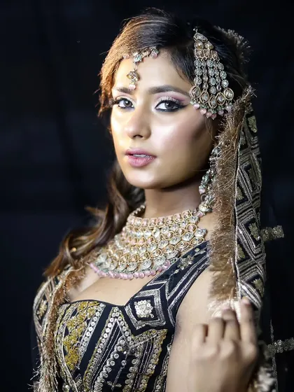 A modern and chic bridal look in a black and gold lehenga. The makeup is soft and glamorous, with a focus on glowing skin and a subtle pink eyeshadow.