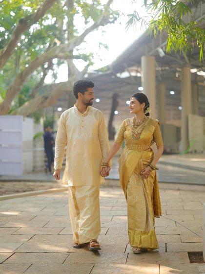 Walking hand-in-hand into their future. This wide shot captures the elegance of the South Indian bride's complete look, from her golden saree to her traditional hairstyle.