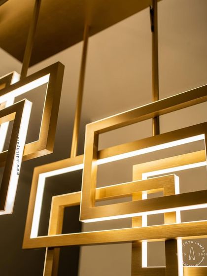 A multi-layered chandelier composed of intersecting rectangular frames with a brushed gold finish. The integrated LEDs cast a warm, ambient light, creating a dynamic and architectural statement piece for modern interiors.