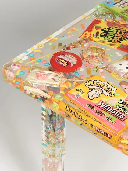 A close-up detail of the candy-filled resin table, showing the texture and variety of sweets like Warheads and Hubba Bubba bubble tape preserved within the piece.