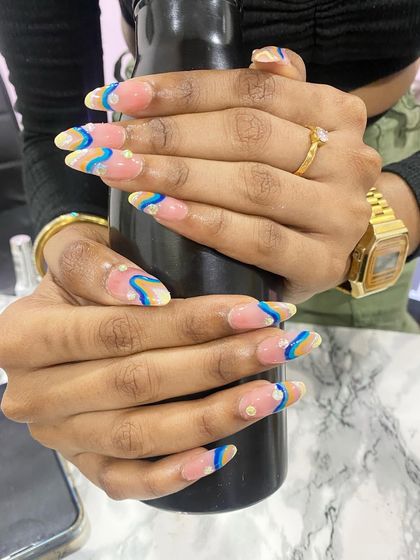 This student's work showcases a trendy, abstract design on long almond-shaped nails. The wavy lines in blue and yellow create a playful, artistic look, accented with small pearls.