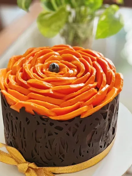 A rich chocolate cake wrapped in an intricate chocolate lace collar and topped with a beautiful mango rose. This design combines intense chocolate flavor with the freshness of mango.