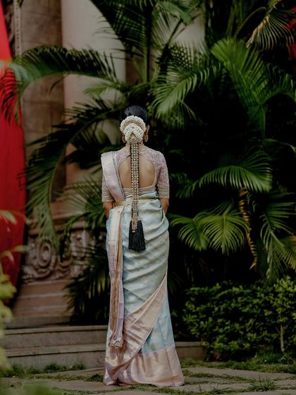 A view from the back, showcasing the bride's elaborate hairstyle and the beautiful drape of her pastel silk saree.