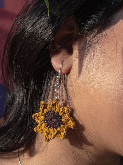 A close-up of the sunflower earring being worn. The chain adds a bit of length and movement to the design.