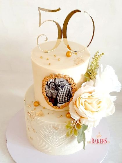 A gorgeous golden anniversary cake in a classic white and gold combination. This no-fondant design features a delicate stencil pattern on the bottom tier and a framed edible photo of the happy couple.