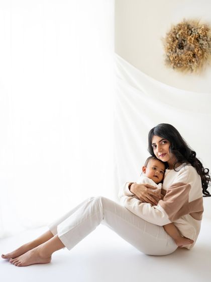 A serene portrait of a mother holding her baby. The soft, natural light from the window and the neutral tones create a peaceful and timeless image.