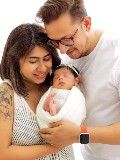 A sweet family photo capturing the parents' affection for their newborn. The mother's floral tattoo adds a modern and personal touch to this classic portrait.
