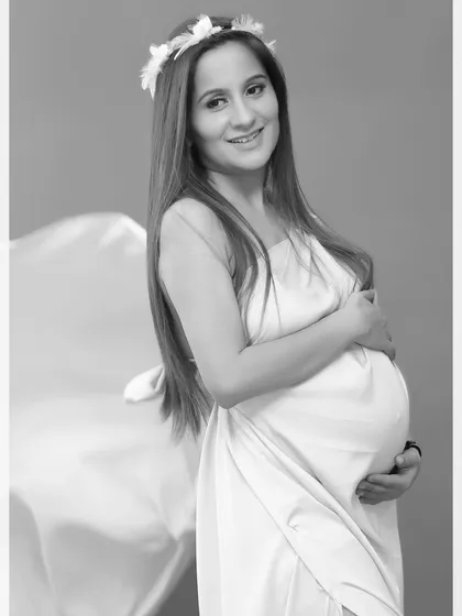 A classic black and white portrait of a smiling mother-to-be in a simple white dress with a floral crown, creating a fresh and timeless image.