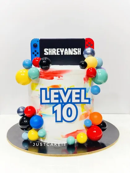 A "Level 10" gaming-themed cake with a Nintendo Switch-style topper. The abstract colors and bubble accents make it a modern and fun design.