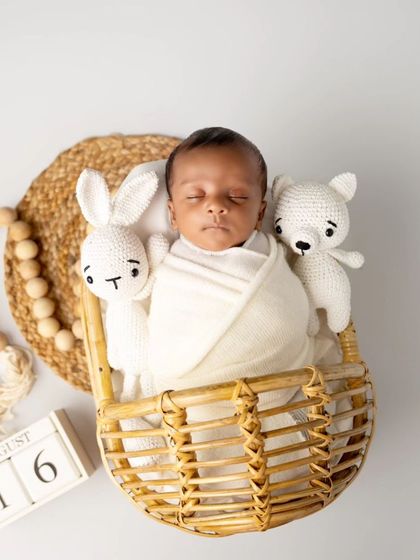 A classic and timeless newborn portrait. The baby is swaddled snugly in a basket with neutral tones and soft textures, focusing purely on his peaceful expression.