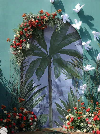 A striking photo backdrop combining a painted palm print with an arch of real red florals and whimsical white butterflies.