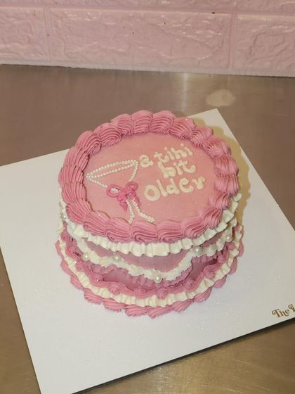 A tiny bit older and a whole lot sweeter. This tiered pink and white cake features vintage frills, pearl details, and a martini glass illustration for a fun 21st birthday.