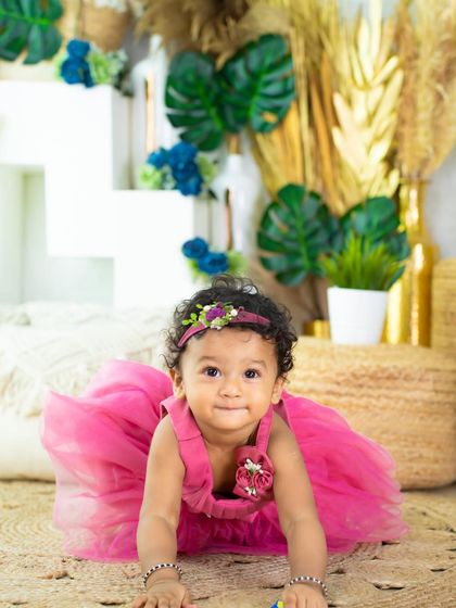 A sweet crawling pose from a one-year-old girl in a pink dress, captured during her pre-birthday session.