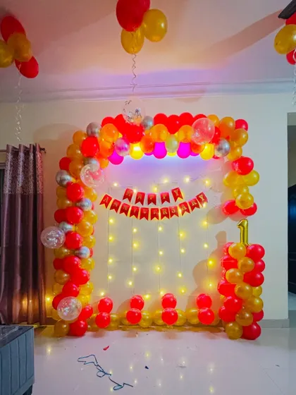 A bright and cheerful first birthday arch in red and yellow, with a fairy light backdrop.