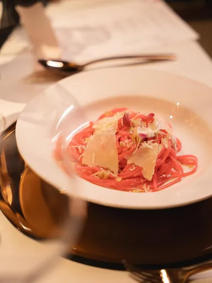 The pink pasta revealed after the smoke has cleared, garnished with cheese and edible flowers. The final dish is both beautiful and delicious.