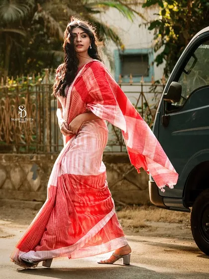 A dynamic walking shot of a model in a red and white handloom saree. The movement of the saree's 'pallu' adds a graceful flow to the image.