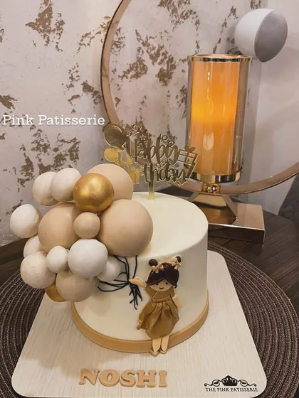 An elegant and modern cake featuring a stylized doll holding a bouquet of balloons. The neutral color palette makes it perfect for a chic celebration.