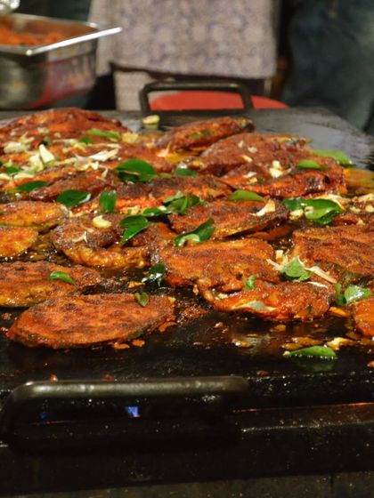 Fresh fish being pan-fried on a large tawa, a classic preparation method in Malabar cuisine. The sight and sound of the sizzling fish, seasoned with fragrant spices, was a highlight of our culinary event.