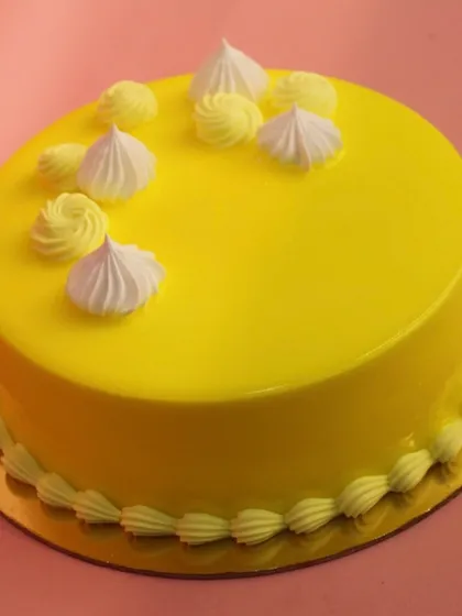 A pineapple cake with a smooth, glossy yellow glaze and delicate meringue-style piping. A sunny and cheerful dessert.