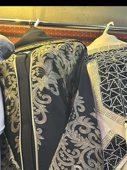For those who love a bold statement, this black abaya with heavy gold embroidery is a showstopper. Next to it is another piece with a geometric black and white pattern.