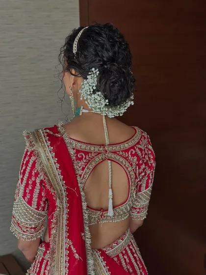 A detailed shot of the bridal hairstyle, featuring a beautiful curly bun adorned with baby's breath, perfectly complementing her red lehenga and the keyhole back design of her blouse.