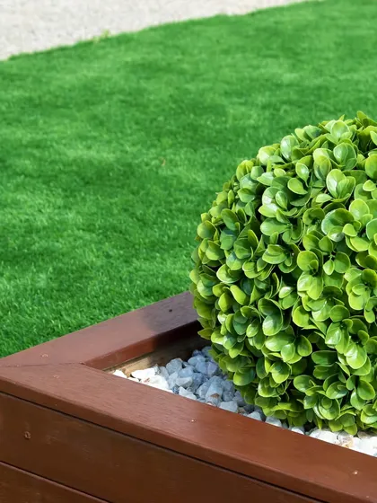This image shows how well artificial grass pairs with other landscaping elements. The clean edge of the turf against the wooden planter and decorative stones creates a sharp, well-defined look in the garden.
