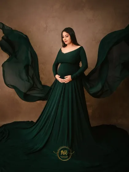 A classic standing portrait in an elegant, long-sleeved emerald green gown. The flowing fabric is expertly tossed to create a sense of movement and grace.
