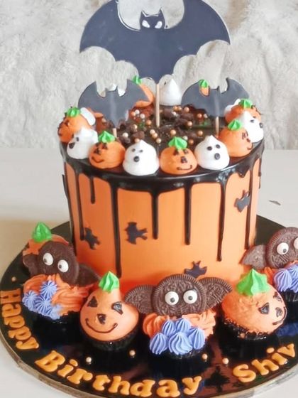 A fun Halloween birthday cake and matching cupcakes, decorated with bats, pumpkins, and ghosts.