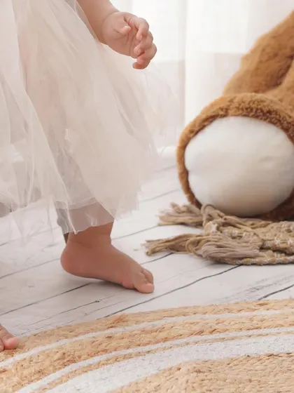 A detail shot focusing on a baby girl's bare feet and tulle dress next to a large teddy bear, adding a touch of innocence to her birthday photos.