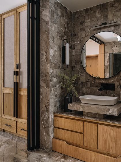 This bathroom in Cocoon House is a rich tapestry of textures. We combined heavily veined grey marble walls with a light wood vanity and a fabric-paneled wardrobe, creating a luxurious and tactile space that feels both modern and timeless.