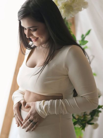 A close-up portrait filled with love. The mother-to-be smiles down at her belly, her hands forming a heart, a simple and beautiful expression of her affection for her unborn child.