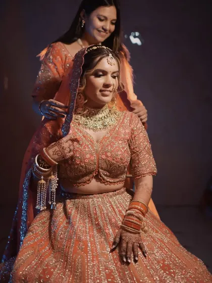 A sister helps place the dupatta, a traditional and emotional part of the getting-ready process. The warm and cool lighting adds a cinematic feel to this beautiful moment.