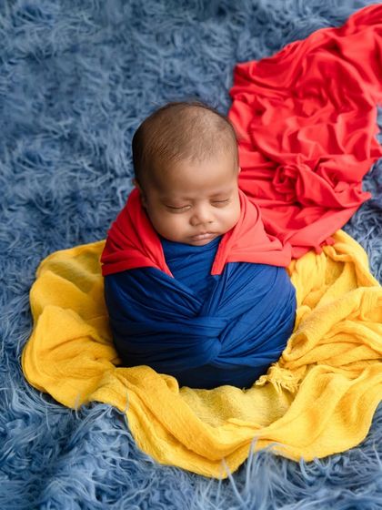 A fun take on a superhero theme, with a newborn swaddled in blue and red wraps to resemble Superman's costume.