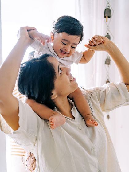 A mother lifting her laughing baby, with light streaming in from the window. A joyful and light-filled image.