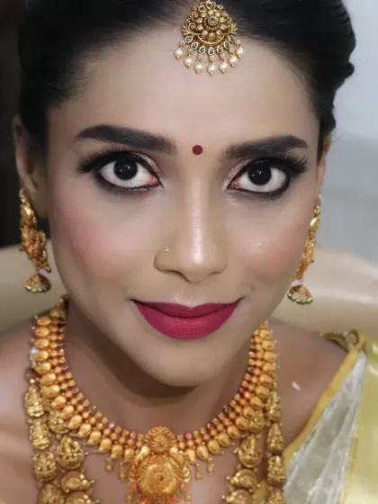 A happy and radiant South Indian bride. Her makeup features bold, defined eyes and a beautiful smile, showcasing the joy of her wedding day. The look is completed with traditional gold jewellery.
