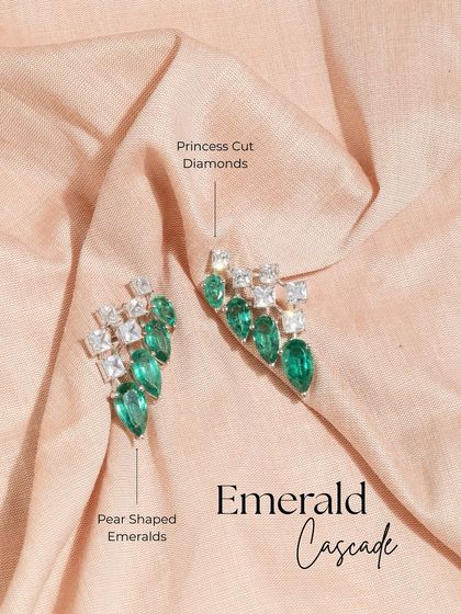 A product shot of the Emerald Cascade earrings against a soft fabric, highlighting the contrast between the sharp diamond cuts and the vibrant green of the emeralds.