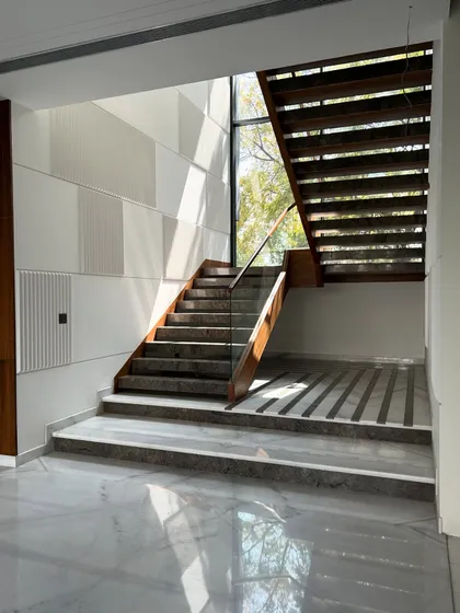 A wider view of the Gulmohar Farmhouse staircase, showing how it is bathed in natural light from a large window, highlighting the different materials and textures.