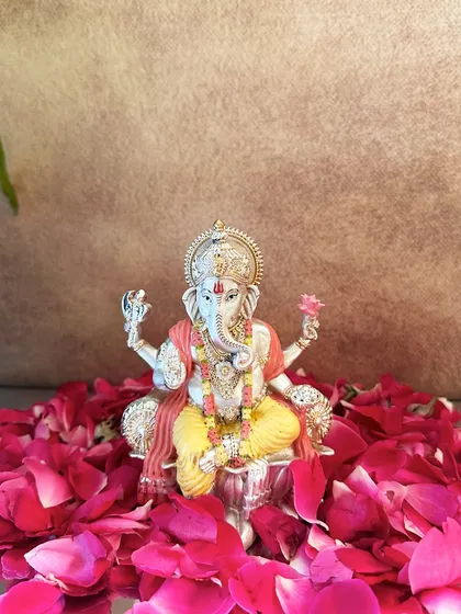 A beautifully hand-painted silver-plated Ganesha idol, surrounded by a bed of fresh rose petals. The soft colors and intricate details make it a truly special piece.