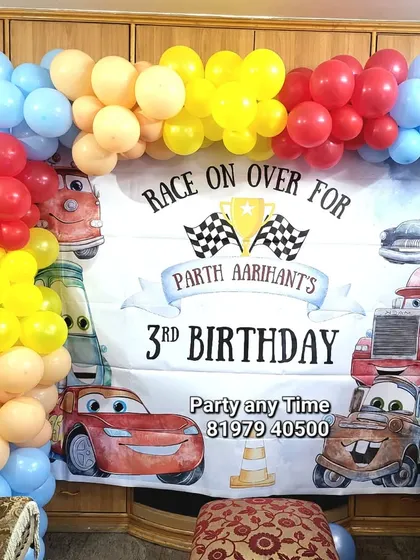 A simple car-themed decoration for a 3rd birthday. This setup uses a printed banner with characters from the movie 'Cars' and a colorful balloon garland.