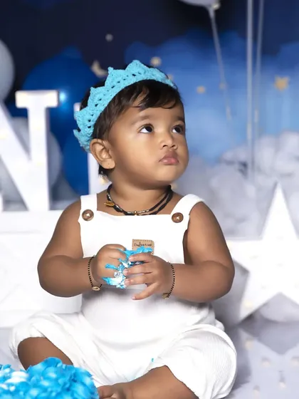 A thoughtful moment captured during a first birthday cake smash. Even with a bit of blue frosting on his hands, this little boy looks adorable in his white overalls and crown.