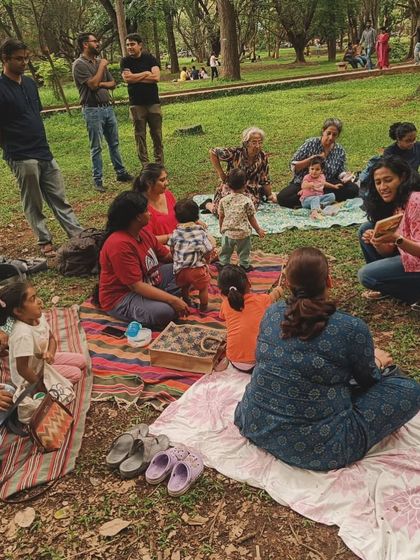 Reading a storybook to an attentive group of toddlers and parents. You can see the mix of ages and the comfortable, casual setting that makes our Cubbon Park storytelling sessions so special for the whole family.