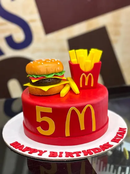 A fun and unique creation, this 3kg cake is designed for a fast-food lover. It features a bright red base with the iconic golden arches and is topped with an incredibly realistic, fully edible fondant burger and fries.