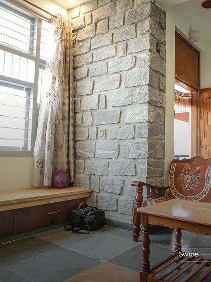 The texture of the exposed stone wall provides a rustic and earthy backdrop to this seating area. The built-in wooden bench with storage underneath is a practical solution that maintains the room's clean, minimal aesthetic.