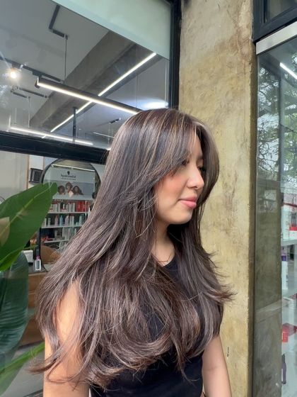 A beautiful lived-in color with ash-toned highlights and face-framing pieces. The long layers and bangs complete this modern look.