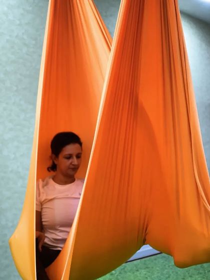A moment of quiet contemplation inside the orange hammock. This shows the meditative aspect of aerial yoga, where the silk cocoon provides a safe space for introspection.