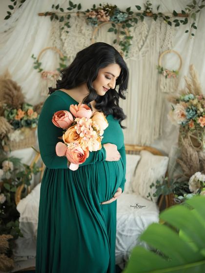 A serene portrait of a mother-to-be holding a bouquet. The colors of the flowers complement her emerald green gown and the earthy tones of the studio.