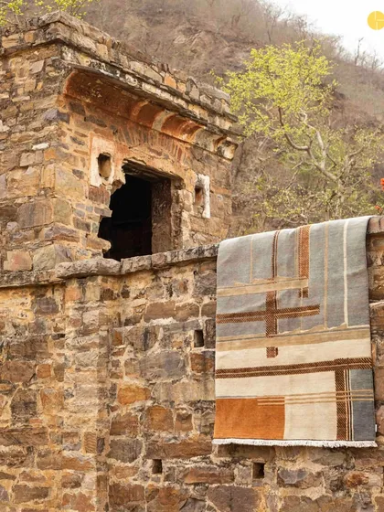 A rug from the collection draped over a historic stone wall, creating a dialogue between the new design and the old structure.