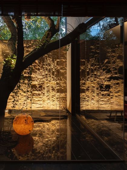 A glass-enclosed courtyard at KEUS, where an old tree is preserved as a central feature. A glowing orb light adds a contemporary artistic touch, its reflection doubling on the glossy floor.